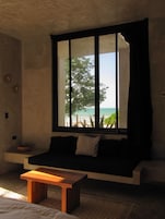 A room with a large window, a sofa, a wooden table, and a view of the beach.
