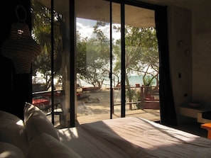 A bedroom with a large window overlooking a beach. - Hotel Amadeo (Isla Holbox)