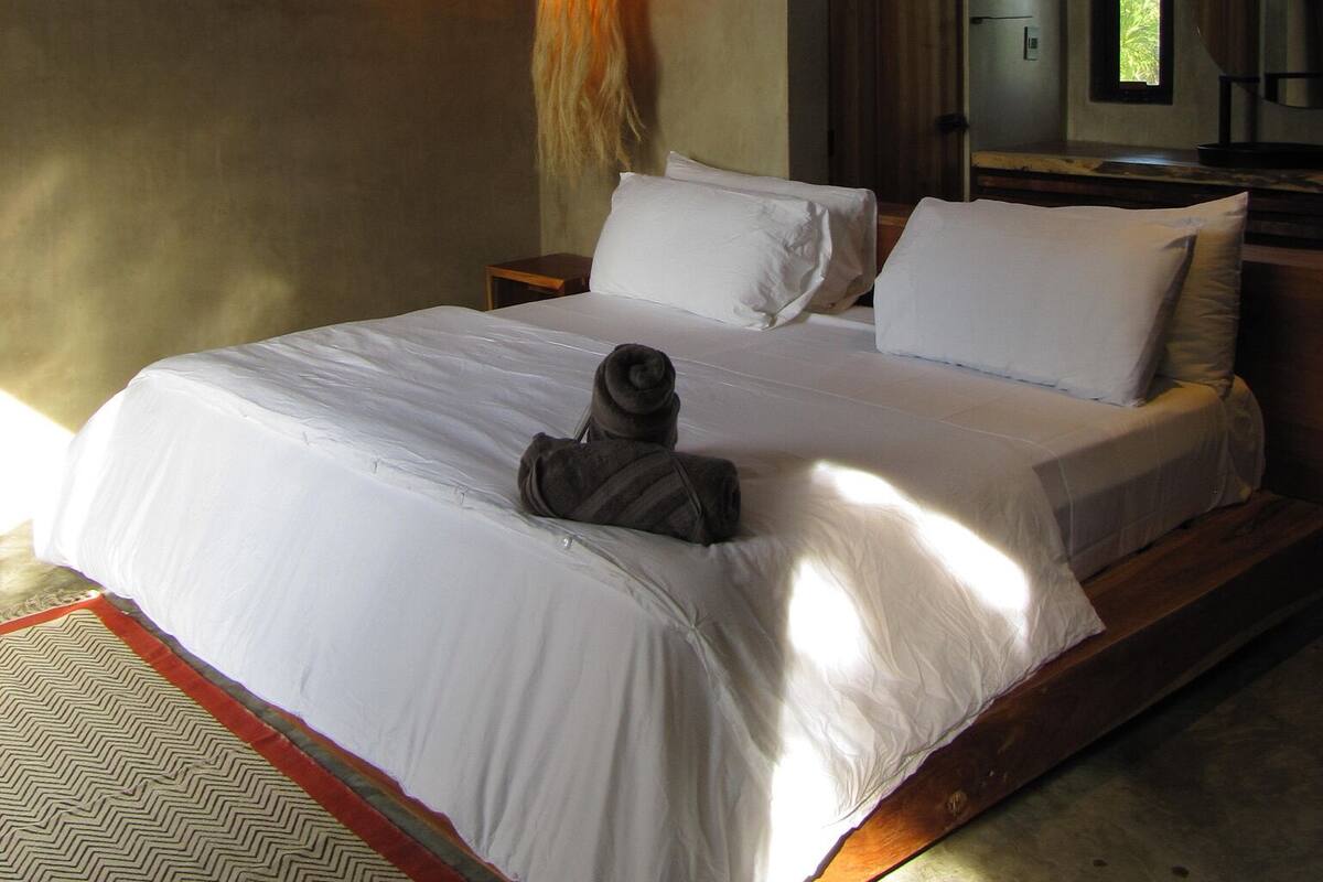 Un dormitorio con cama, lámpara colgante, ventana y espejo.