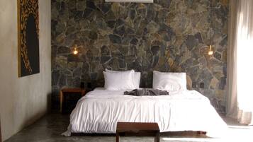 A bedroom with a stone wall, a bed with white bedding, two bedside tables, and a hanging light fixture.