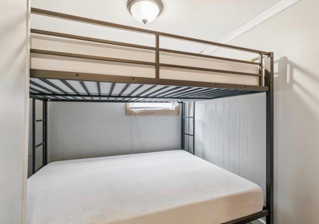 Un lit superposé avec un matelas, une structure en métal et un luminaire fixé au plafond.
