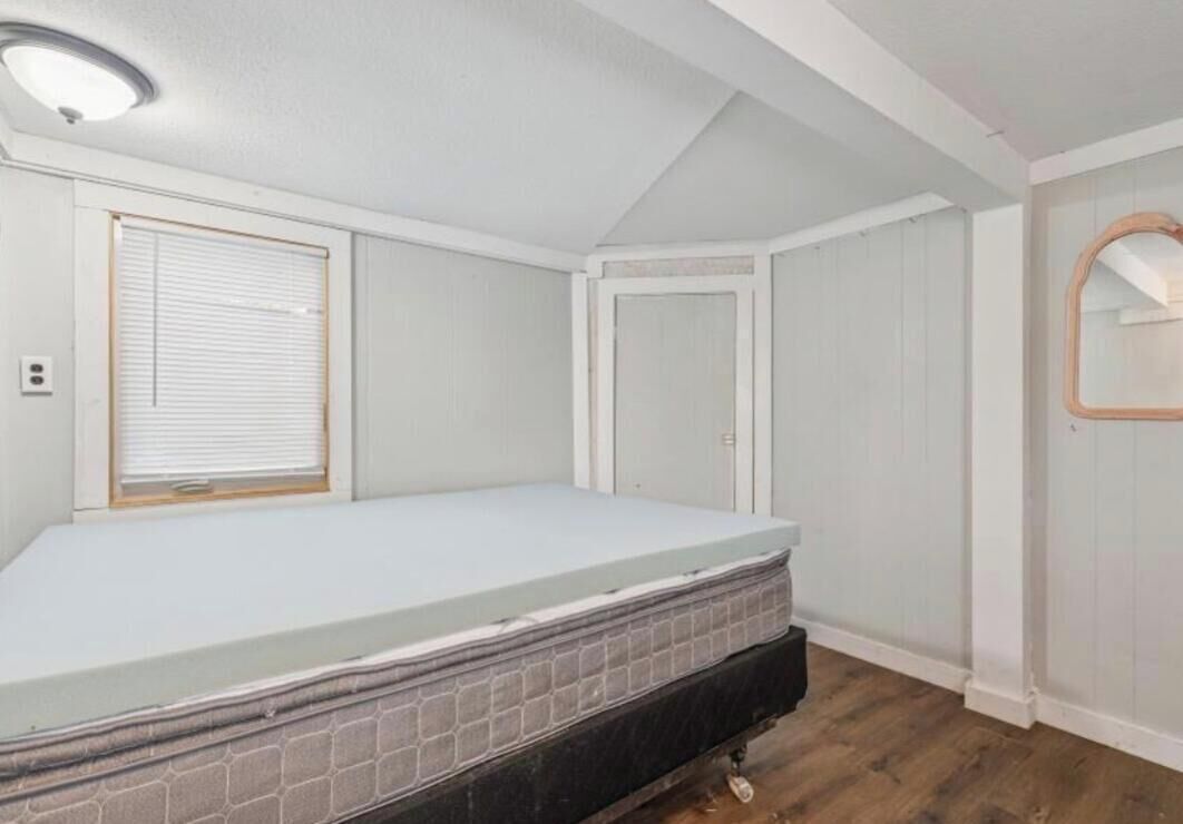 Un dormitorio con una cama individual, una ventana con persianas, una puerta y un espejo en la pared.