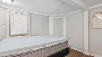 Un dormitorio con una cama individual, una ventana con persianas, una puerta y un espejo en la pared.