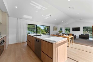 A modern kitchen with a central island, wooden cabinetry, and a dining area with a table and chairs. - Kinloch Retreat (Kinloch)