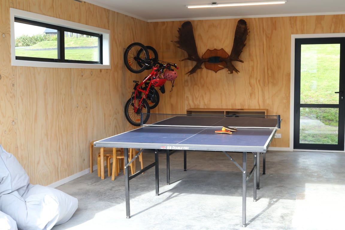 Une table de ping-pong dans une pièce aux murs en bois, un vélo et une grande fenêtre.