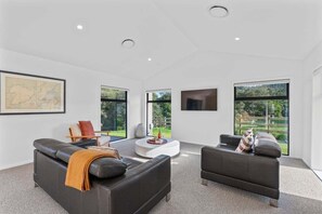 A modern living room with two sofas, a coffee table, and a TV mounted on the wall. - Kinloch Retreat - stay n play, golf, hike & bike (Kinloch)
