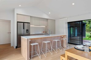 A modern kitchen with a central island, bar stools, and a view of the outdoors. - Kinloch Retreat - stay n play, golf, hike & bike (Kinloch)