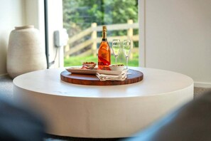 A round white table with a bottle and glasses, a bowl of food, and a white vase in a room with a window view. - Kinloch Retreat - stay n play, golf, hike & bike (Kinloch)