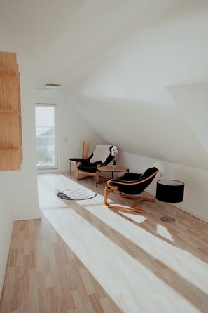 Una habitación moderna y minimalista con techo inclinado, suelo de madera y dos sillones de cuero negro.