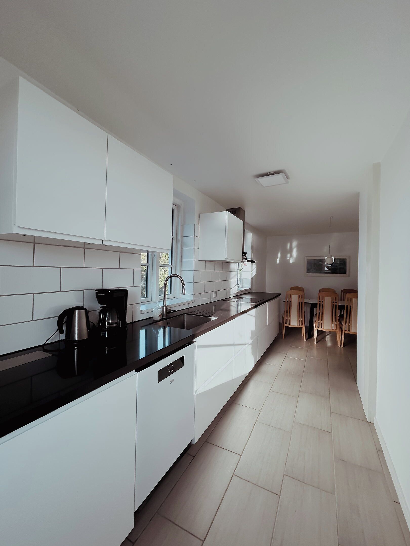 A modern kitchen with white cabinets, a black countertop, and a dining area with wooden chairs.