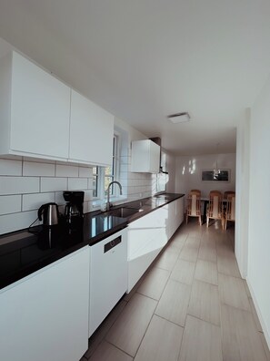 Una cocina moderna con armarios blancos, encimera negra y zona de comedor con sillas de madera.
