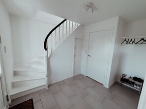 Interior claro com escada, porta e sapateira.