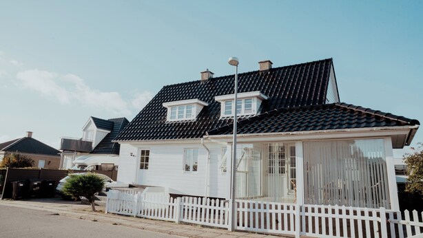 Une maison blanche avec un toit noir, une clôture blanche faite de piquets et un ciel dégagé.