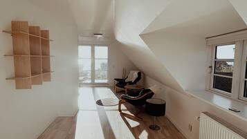 A spacious room with a sloped ceiling, a radiator, a window, and a seating area with a chair and a table.