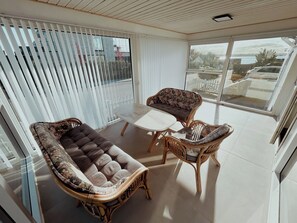 Un balcón con mobiliario de mimbre, una puerta de cristal y vista al mar.