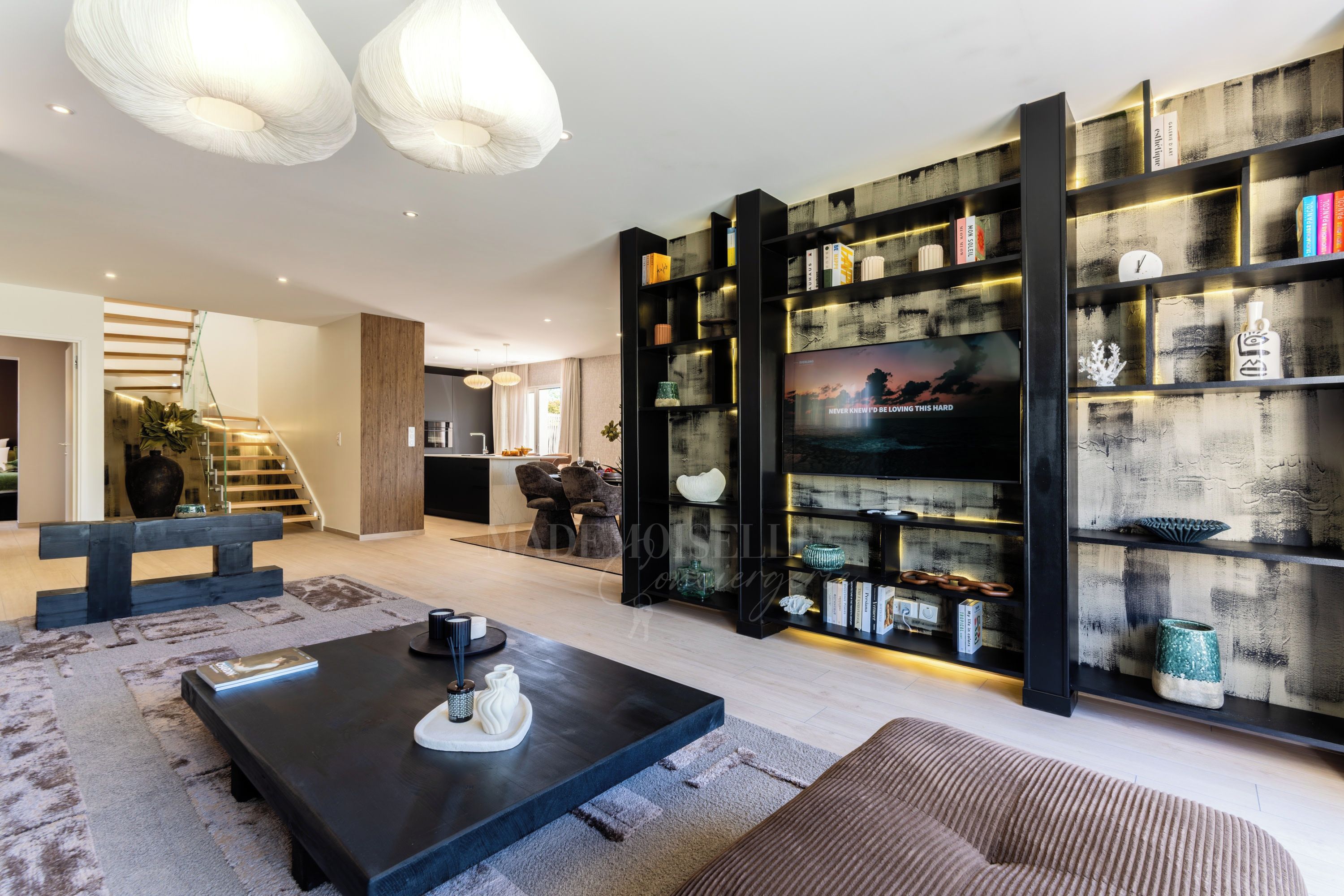 A modern living room with a black coffee table, a sofa, and a bookshelf filled with books and decorative items.