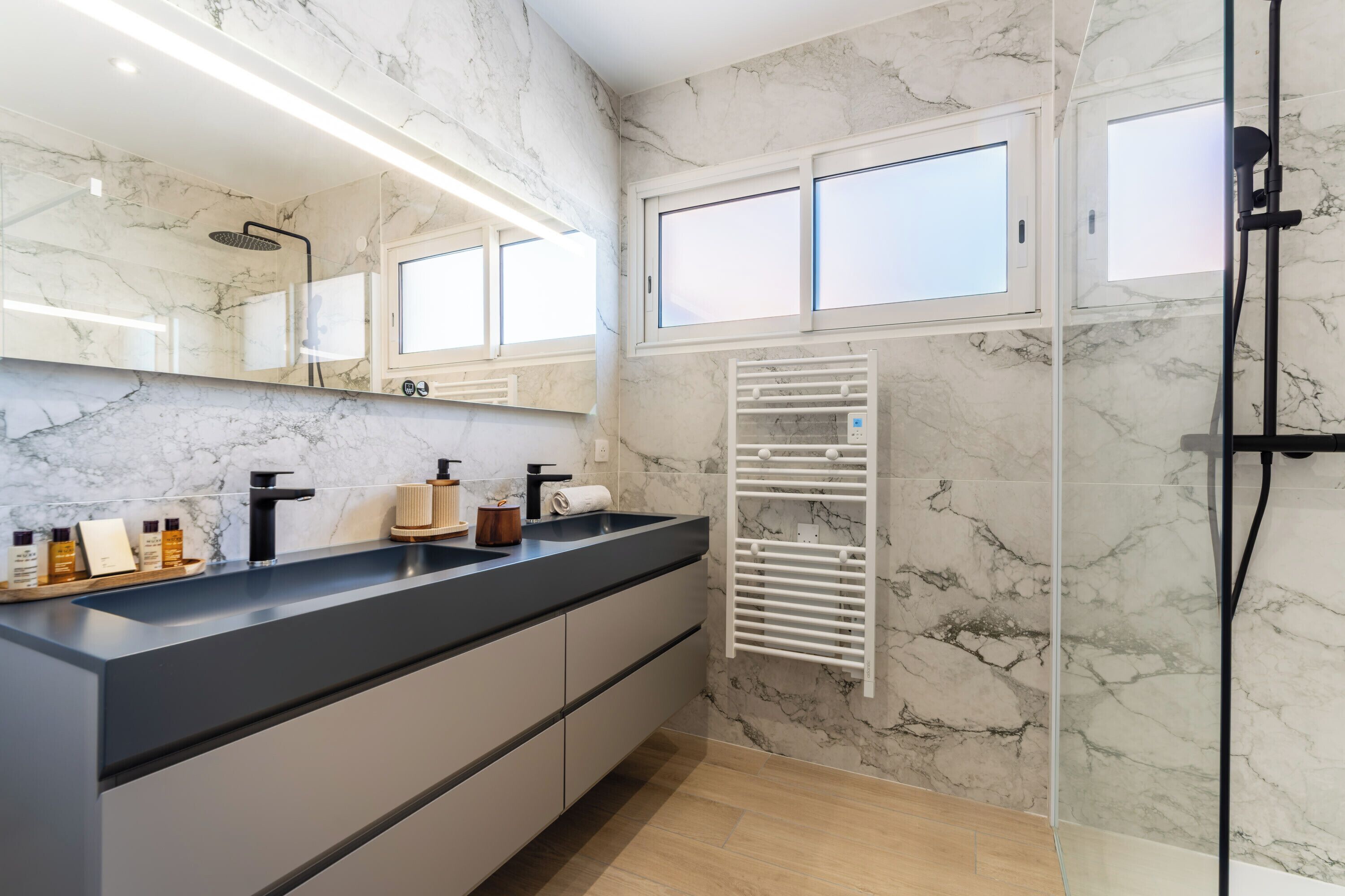 Un baño con pared de mármol, un lavabo negro, un espejo, un perchero para toallas y una ventana.