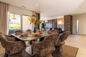 A dining area with a table set for four, surrounded by upholstered chairs. - Villa Maya · Rooftop beach access heated pool (Agde)