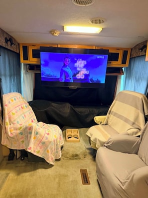 A room with a television, a sofa, a chair, and a blanket.