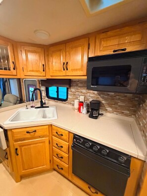 A compact RV kitchen with wooden cabinets, a sink, a microwave, and a stove. - Comfortable home on wheels (Gadsden)