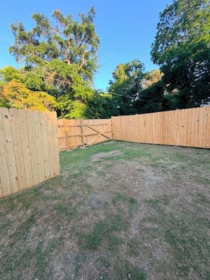 A fenced backyard with a grassy area and trees in the background.