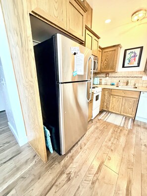 Een keuken met houten kasten, een roestvrijstalen koelkast, een betegelde spatwand en een houten vloer.