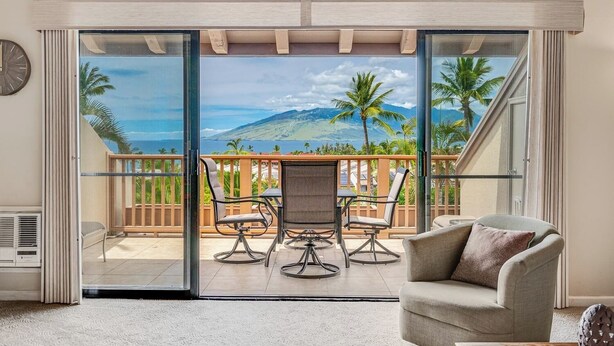 Una habitación con puerta de cristal corredera que da a un balcón con vistas a una montaña y palmeras.