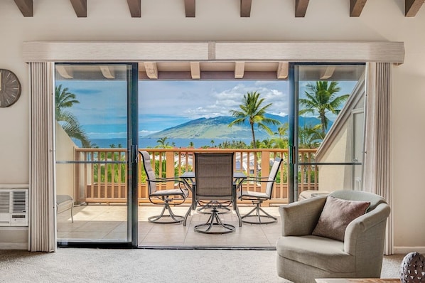 A room with a sliding glass door leading to a balcony with a view of a mountain and palm trees. - Experience Paradise, 2-Bed Kihei Condo with A/C and New June 2026 Ownership J214 (Kihei)