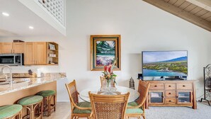 Una cocina moderna con microondas, armarios de madera y una zona de comedor con sillas de mimbre y una mesa de vidrio.