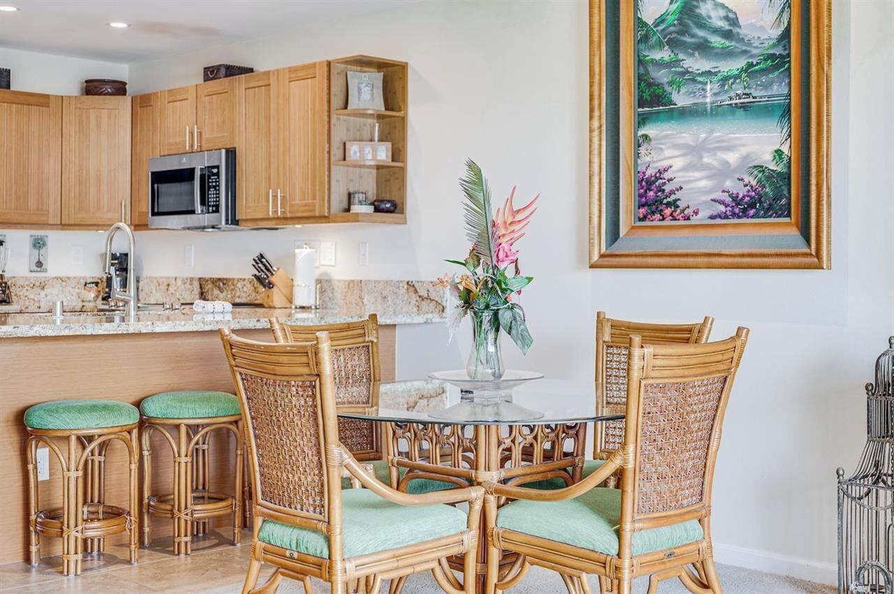 Una cocina con armarios de madera, microondas, una mesa de comedor con sillas y un cuadro en la pared.