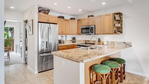 Una cocina moderna con encimeras de granito, electrodomésticos de acero inoxidable, armarios de madera y una isla central con taburetes de bar.