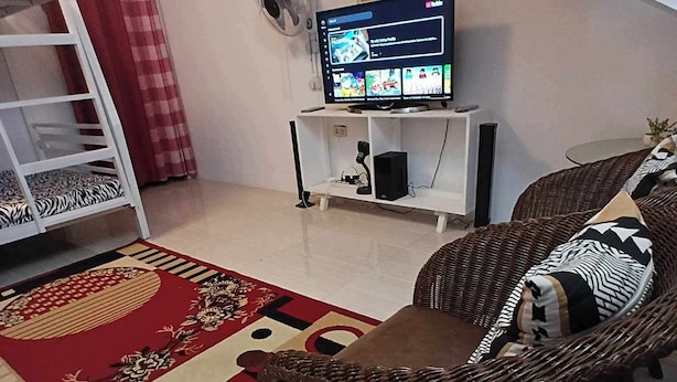 A living room with a sofa, a TV, a fan, a ladder, and a patterned rug. - Bale Magalang (Magalang)