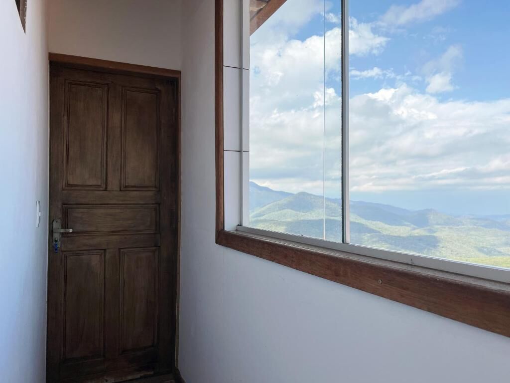 A room with a wooden door and a large window offering a view of distant hills.