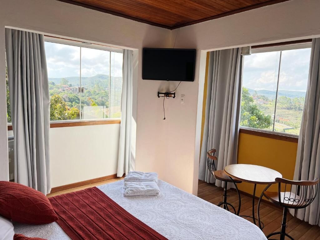 Habitación de hotel con cama, televisor montado en la pared, balcón con mesa y sillas, y vista al paisaje.
