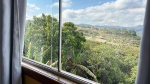 A view from a window overlooking a lush landscape with trees and distant hills. - Pousada Vista de Lavras (Ouro Preto)