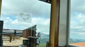 A view from a window with a wooden railing, a sign with text, and a mountainous landscape. - Pousada Vista de Lavras (Ouro Preto)