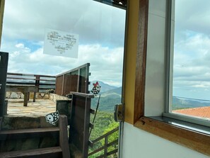 Vista desde una ventana con barandilla de madera, un cartel con texto y un paisaje montañoso.