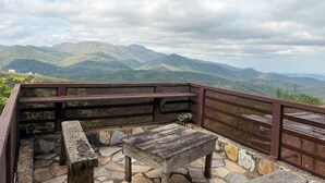 A wooden bench and table set on a stone patio with a view of green mountains. - Pousada Vista de Lavras (Ouro Preto)
