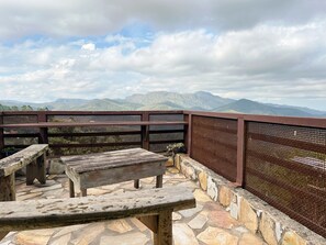 A wooden bench and table on a stone-tiled patio with a view of mountains.