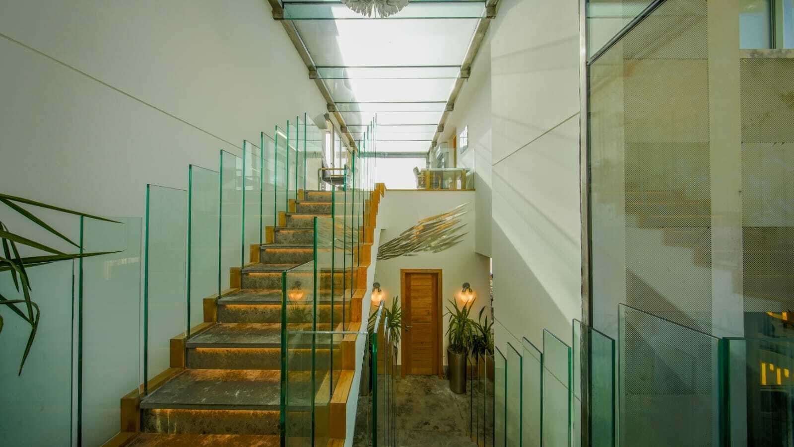 A modern staircase with glass railings, a wooden door at the bottom, and a ceiling light fixture.