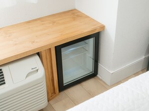 Ein schmaler Raum mit einem Holzbüro, einer kleinen Vitrine mit schwarzem Rahmen und einem weißen Gerät.