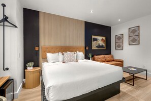 Quarto de hotel moderno com uma cama grande, um sofá, uma mesinha e uma prateleira fixada na parede.