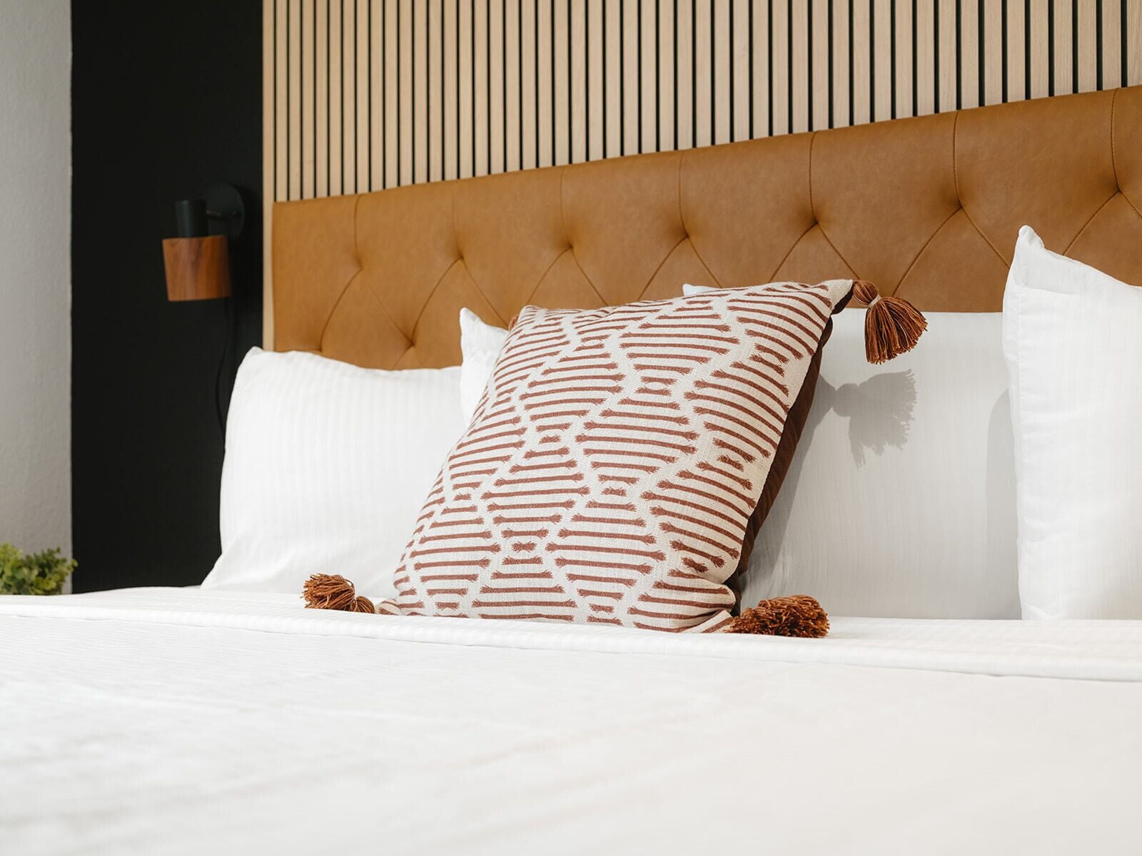 Ein Bett mit einer karabinierten Kopfteil, weißer Bettwäsche und gemusterten Kissen.