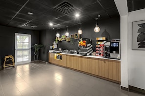 Moderni kahvila, jossa on puinen tiski, espressokoneet ja katosta roikkuvat riippuvalaisimet.