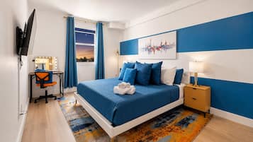 Ein Schlafzimmer mit Bett, Schreibtisch mit Spiegel, Nachttisch und Wandfernseher.