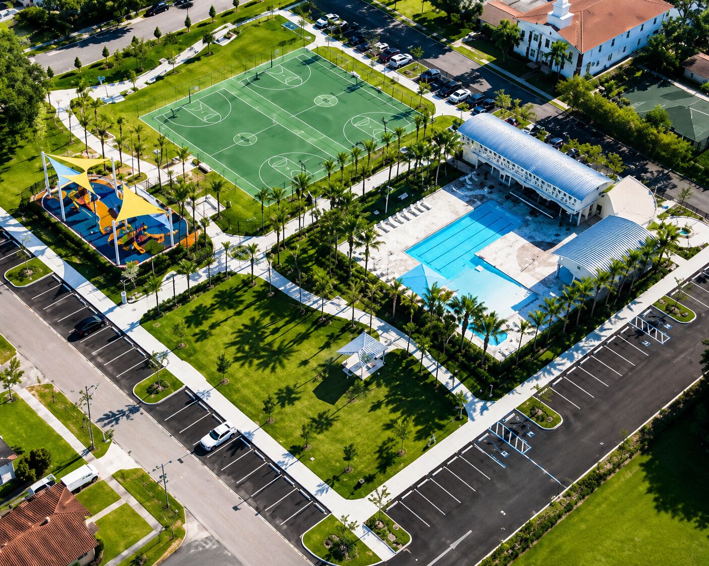Vue aérienne d’un complexe sportif comprenant un terrain de basket-ball, une piscine et un pavillon couvert.