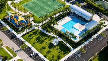 Vue aérienne d’un complexe sportif comprenant un terrain de basket-ball, une piscine et un pavillon couvert.
