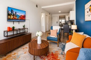 A modern living room with a TV, sofa, coffee table, and a dining area with a kitchen in the background. - Costal Retreat+Pool Near Hollywood Beach & FIFA WC (Hallandale Beach)