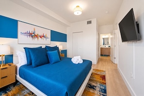A hotel room with a large bed, a cityscape painting, a flat-screen TV, and a bathroom visible through an open door. - Costal Retreat+Pool Near Hollywood Beach & FIFA WC (Hallandale Beach)