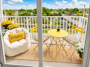 A balcony with a white cushioned chair, a small yellow table, and colorful cushions. - Costal Retreat+Pool Near Hollywood Beach & FIFA WC (Hallandale Beach)